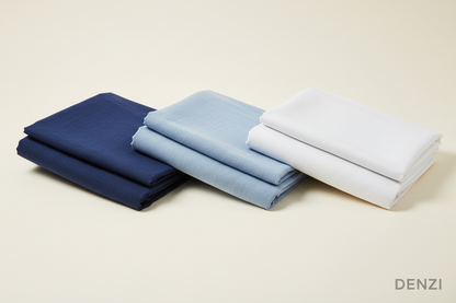 Create a 100% realistic single image featuring three men’s unstitched cotton suits placed neatly side by side. The colors should be Navy Blue, Sky Blue, and White. Show full fabric texture clearly with natural lighting. The background should be simple, clean, and elegant to highlight the suits. Add the text ‘DENZI’ at the bottom-right corner of the picture in a minimal, stylish font